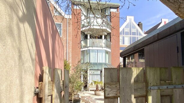 A narrow alleyway with a wooden gate, a brick building with a turret, and a paved path with stepping stones. - Bed and Ontbijt Haddock (Almere)