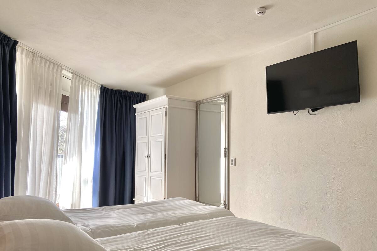 Une chambre d’hôtel avec deux lits, une armoire, une télévision et une fenêtre avec des rideaux.