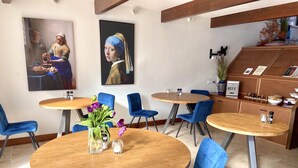 A dining area with round wooden tables and blue upholstered chairs, featuring artwork on the walls and a small bar area with a sign reading "KEY'S". - Bed and Ontbijt Haddock (Almere)