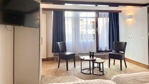 A hotel room with a bed, two chairs, a small table, a TV mounted on the wall, and a window with curtains. - Bed and Ontbijt Haddock (Almere)