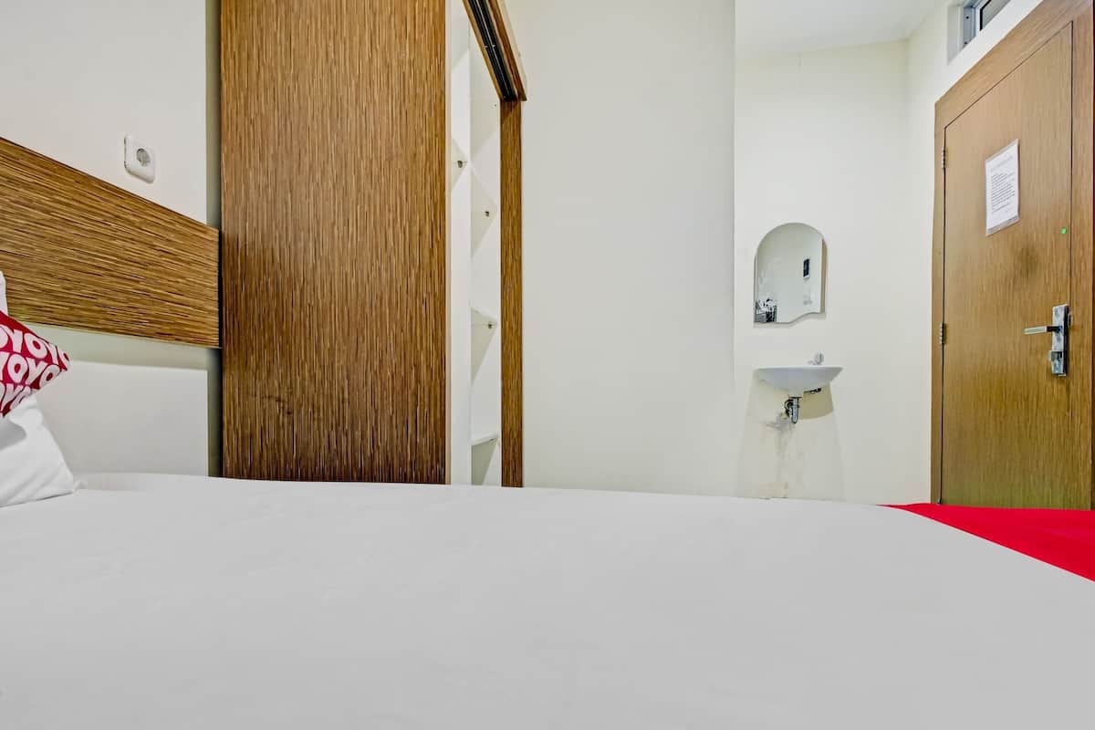 A hotel room with a bed, a wooden wardrobe, a white sink, and a door.