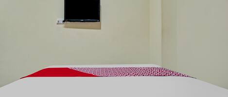 A room with a bed, a small TV mounted on the wall, and a red and white patterned bedspread.