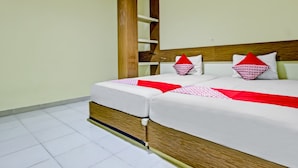 Uma cama de casal com cabeceira de madeira, roupa de cama branca e almofadas decorativas vermelhas.
