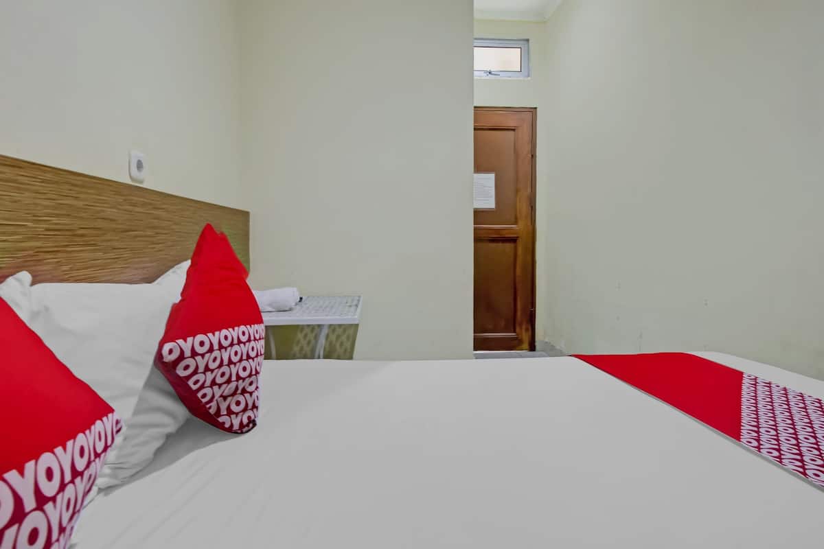 A hotel room with a bed, a wooden headboard, a desk with a chair, and a door.