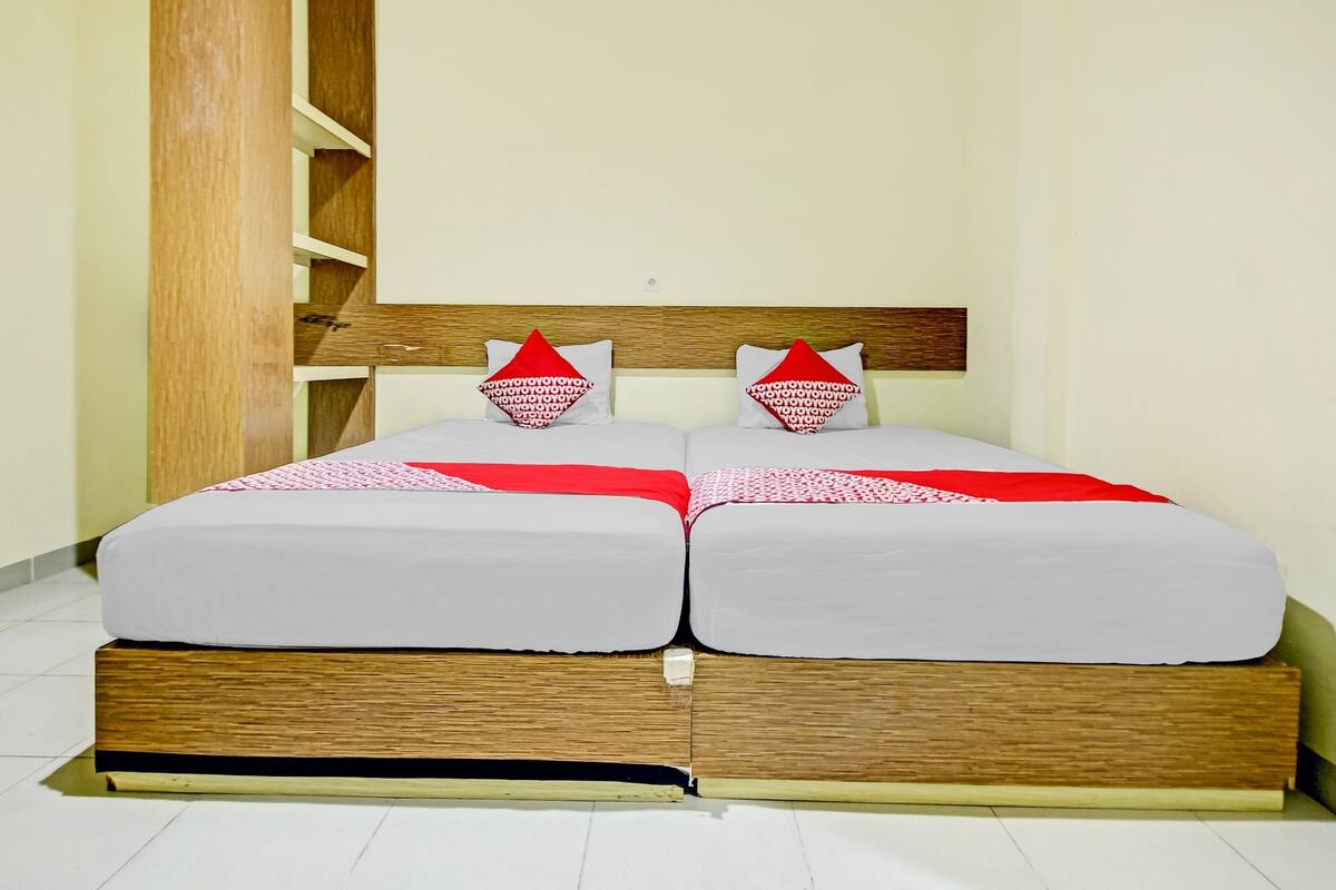 A double bed with a wooden headboard, two pillows with red and white patterns, and a red and white bedspread.