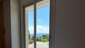 A bedroom with a large bed, a sliding glass door leading to an outdoor deck, and a view of the sea. - Villa with superb sea view, swimming pool, 350 metres from the beach, air conditioning, garden (LE LAVANDOU)