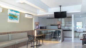 A modern kitchen with a central island, a dining area with a sofa and chairs, and a TV mounted on the wall. - OYO 3811 Best Inn Hotel (Jakarta)