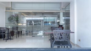 A modern dining area with glass partitions, black and white chairs, and a visible kitchen area in the background. - OYO 3811 Best Inn Hotel (Jakarta)