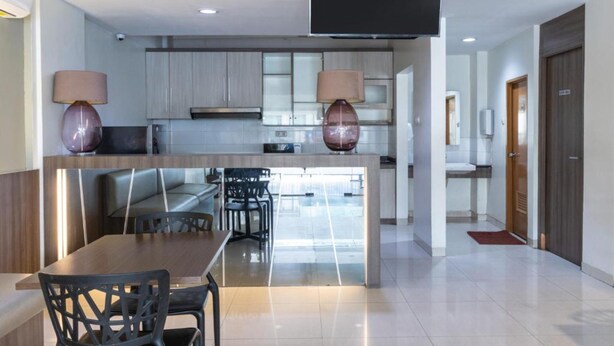 A modern kitchen with a central island, a dining area with a table and chairs, and a flat-screen TV mounted on the wall. - OYO 3811 Best Inn Hotel (Jakarta)