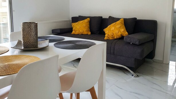 Ein modernes Wohnzimmer mit grauem Sofa, gelben Kissen, weißem Esstisch und Untertassen sowie einem minimalistischen Design.