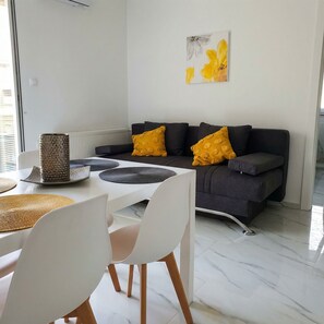 A modern living room with a grey sofa, yellow cushions, a white dining table with placemats, and a minimalist design.