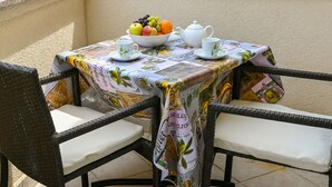 Ein Tisch mit Obstschale, Teekanne und Tassen auf einem Balkon mit Korbstühlen.