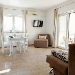 Uma sala de estar moderna com área de jantar, uma TV de tela plana na parede e uma porta de vidro deslizante que dá para uma área externa.