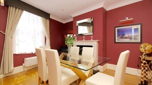 Un comedor con una mesa de vidrio, sillas blancas, un jarrón con flores, una chimenea y un cuadro en la pared.