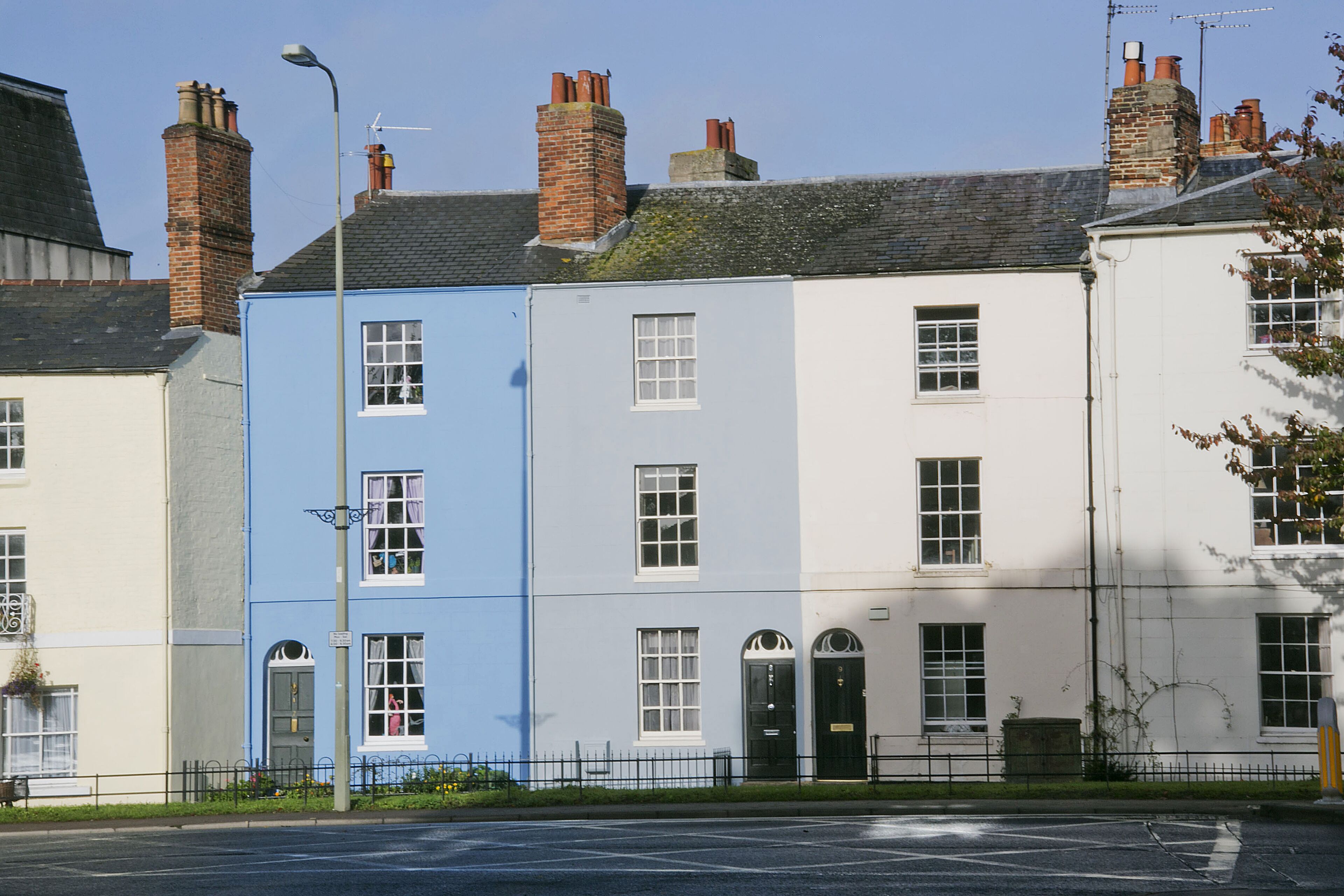 A row of three-story townhouses with distinct colors, a street lamp, and a clear sky.