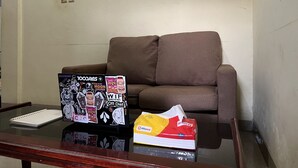 A brown sofa, a glass table with a notebook, and a package of tissues. - SPOT ON 92338 Karin Kost (Karang Intan)