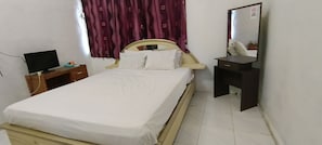 A bed with white bedding, a wooden headboard, a nightstand with a TV, a mirror, and a dark nightstand. - SPOT ON 92338 Karin Kost (Karang Intan)