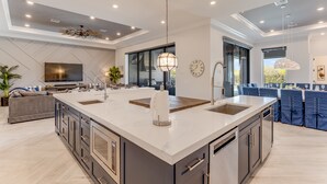 A modern kitchen with a large island, built-in appliances, and a dining area with blue chairs. - Games Room | Theater Room | Kids Bunk Themed Bedrooms | Pool with Golf Course Views (Kissimmee)