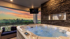 A hot tub with a stone wall backdrop, a mounted TV, and a sofa with a cushion. - Games Room | Theater Room | Kids Bunk Themed Bedrooms | Pool with Golf Course Views (Kissimmee)