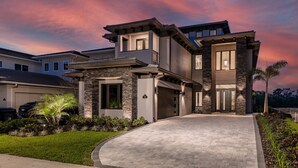 A modern two-story house with a stone facade, a driveway, and a well-maintained lawn. - Games Room | Theater Room | Kids Bunk Themed Bedrooms | Pool with Golf Course Views (Kissimmee)