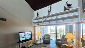 Amplia sala de estar con televisor, asientos cómodos, una mesa de centro de vidrio y un balcón con vistas.
