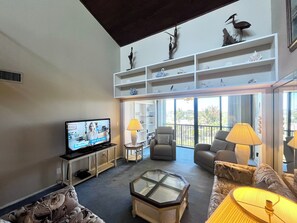 A spacious living room with a television, comfortable seating, a glass coffee table, and a balcony with a view. - BT 3942 Pond View Condo-Welcome to Paradise (Fort Pierce)