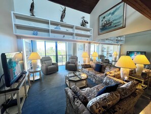 A spacious living area with a large window, comfortable seating, and decorative items on shelves. - BT 3942 Pond View Condo-Welcome to Paradise (Fort Pierce)