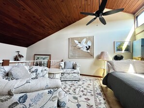 A room with a high ceiling, a ceiling fan, a bed, a sofa, a chair, a table, and artwork on the walls. - BT 3942 Pond View Condo-Welcome to Paradise (Fort Pierce)