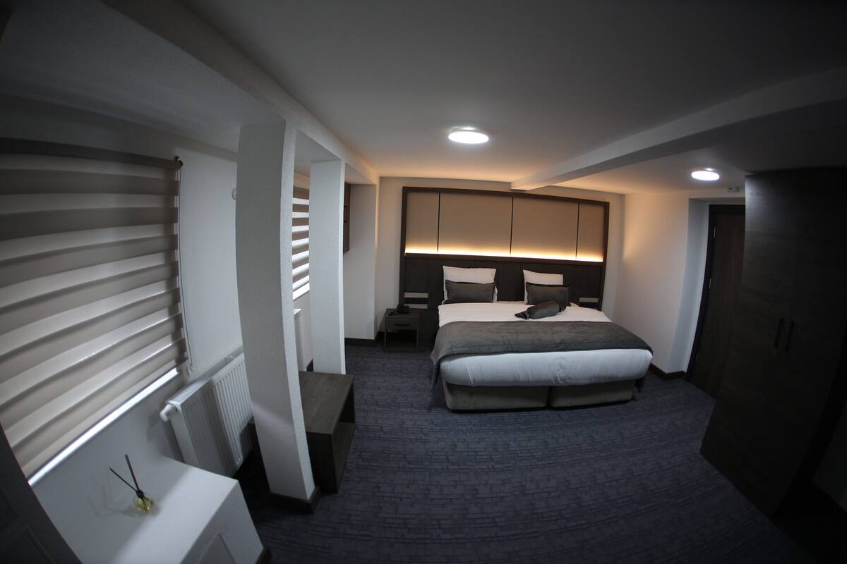 A modern hotel room with a large bed, a bedside table, a nightstand, and a wardrobe.