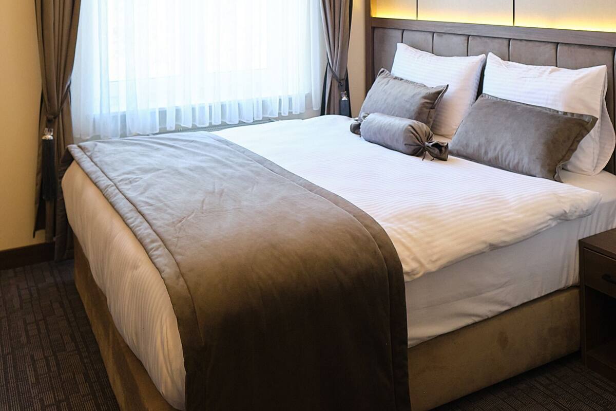 A hotel room with a large bed, curtains, a headboard, and a carpeted floor.