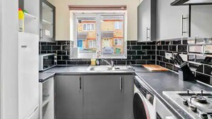 A modern kitchen with grey cabinets, a black countertop, and a window overlooking a residential area. - 4 bed Townhouse- Free Parking (London)