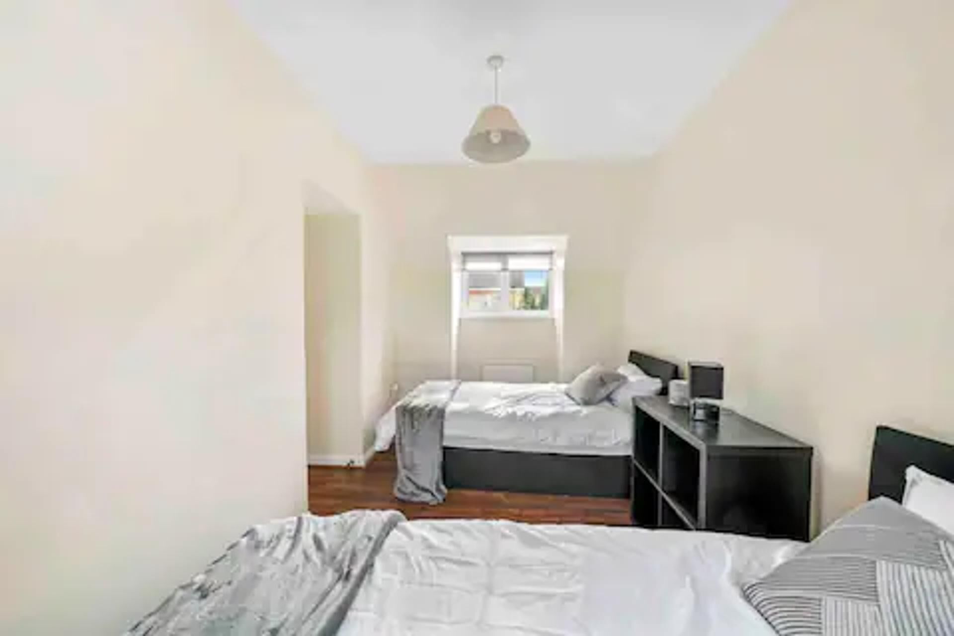 A bedroom with two beds, a window, a desk, and a hanging light fixture.