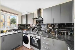 A modern kitchen with grey cabinets, a built-in oven, a washing machine, and a large window.