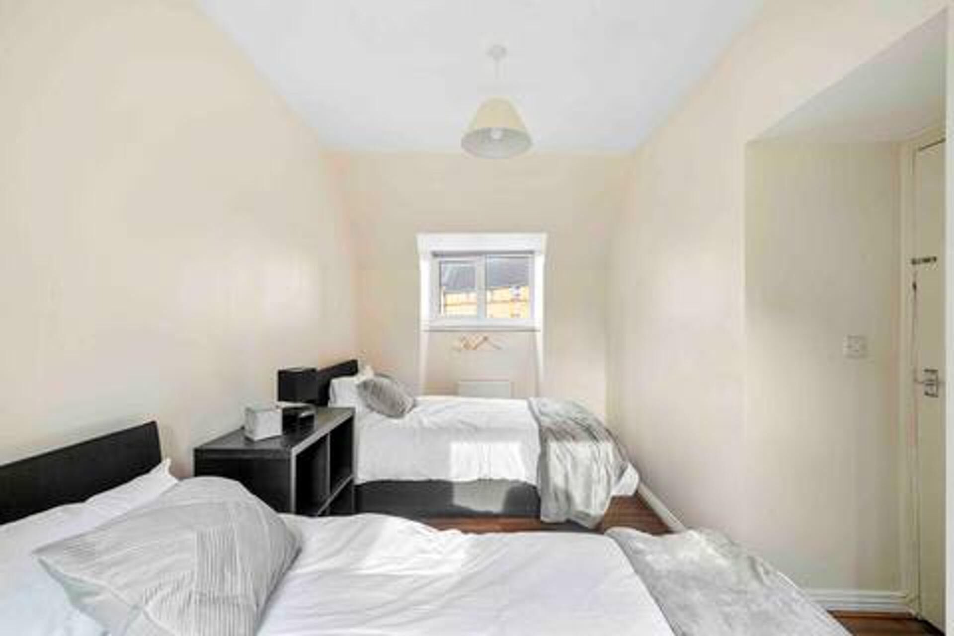 A bedroom with two beds, a window, and a door.