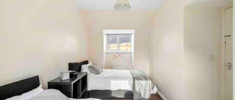 A bedroom with two beds, a window, and a door.