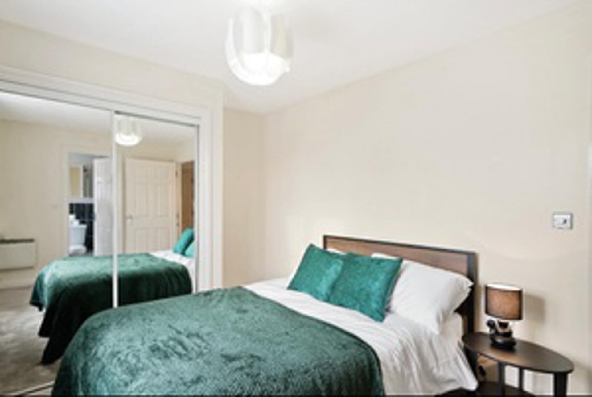 Ein Hotelzimmer mit zwei Betten, einem Nachttisch mit Lampe und einem großen Spiegel.