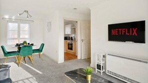 Ett modernt vardagsrum med en matplats, ett kök i bakgrunden och en tv-skärm som visar Netflix-logotypen.