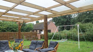 Un patio couvert avec des meubles en osier et une balançoire.