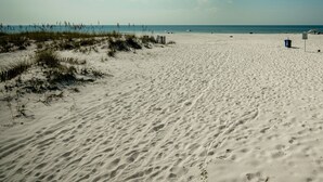 A wide sandy beach with sparse vegetation and a clear sky.