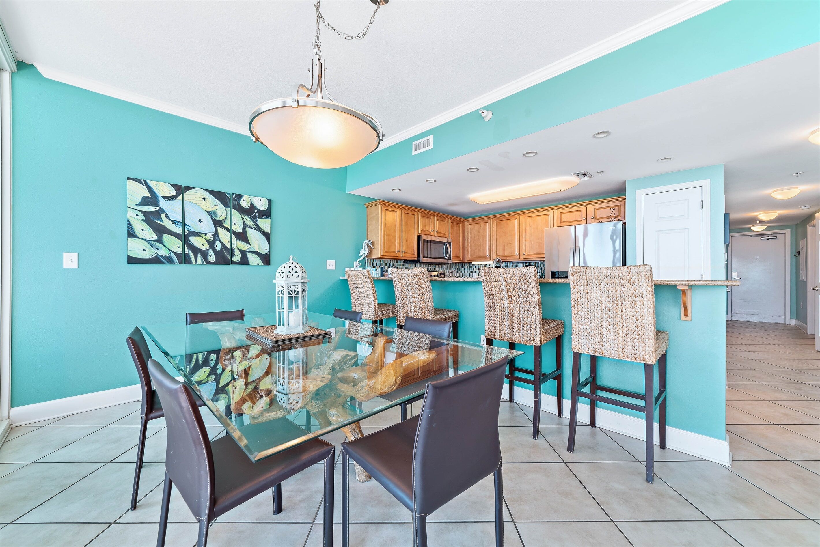 A modern kitchen with teal walls, a glass dining table, and wooden cabinets.