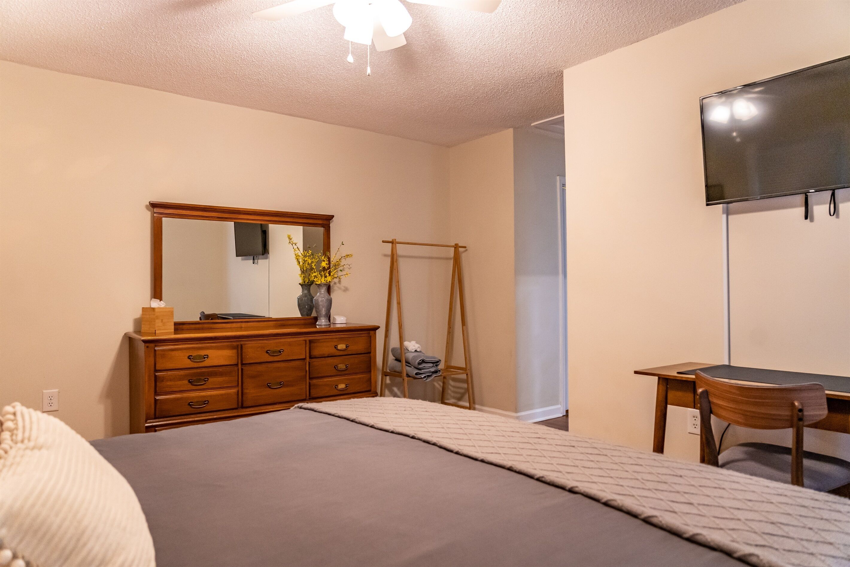 A bedroom with a bed, dresser, mirror, and a TV mounted on the wall.