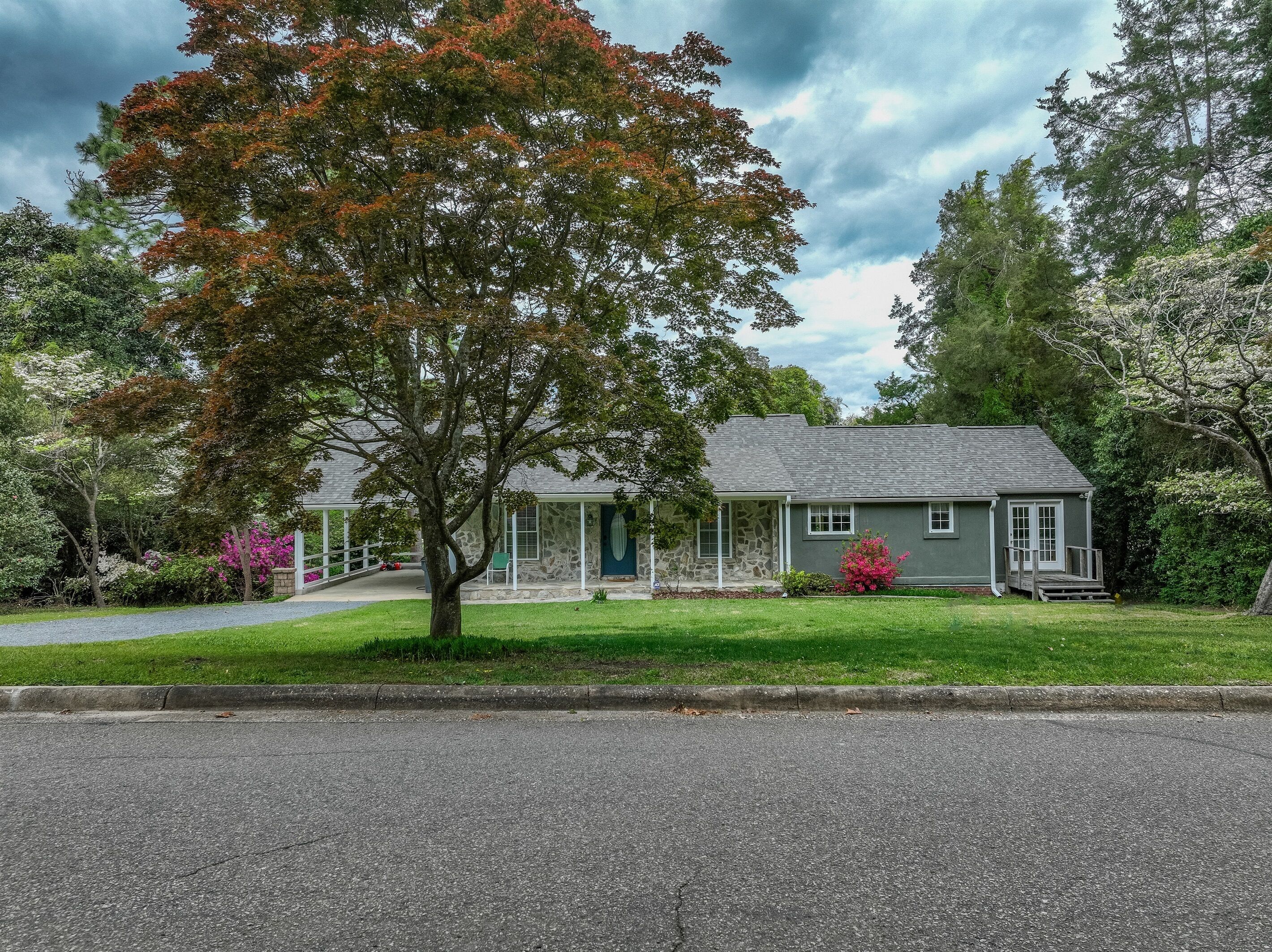 Une maison à deux étages avec une façade en pierre, un porche à l’avant et une pelouse bien entretenue.