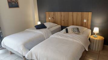 Une chambre d’hôtel avec deux lits simples, une tête de lit en bois, une table de chevet avec une lampe et un tableau encadré au mur.