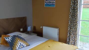 Um quarto com cama, radiador, janela com cortinas e um cartaz na parede.