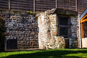 Um edifício de pedra com uma janela e porta, uma pequena área de jardim com relva, e uma vedação de madeira ao fundo.