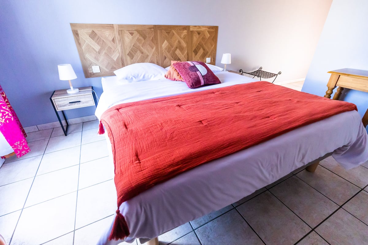 Cama bem arrumada com um cobertor vermelho, cabeceira de madeira e duas mesas de cabeceira com abajures.