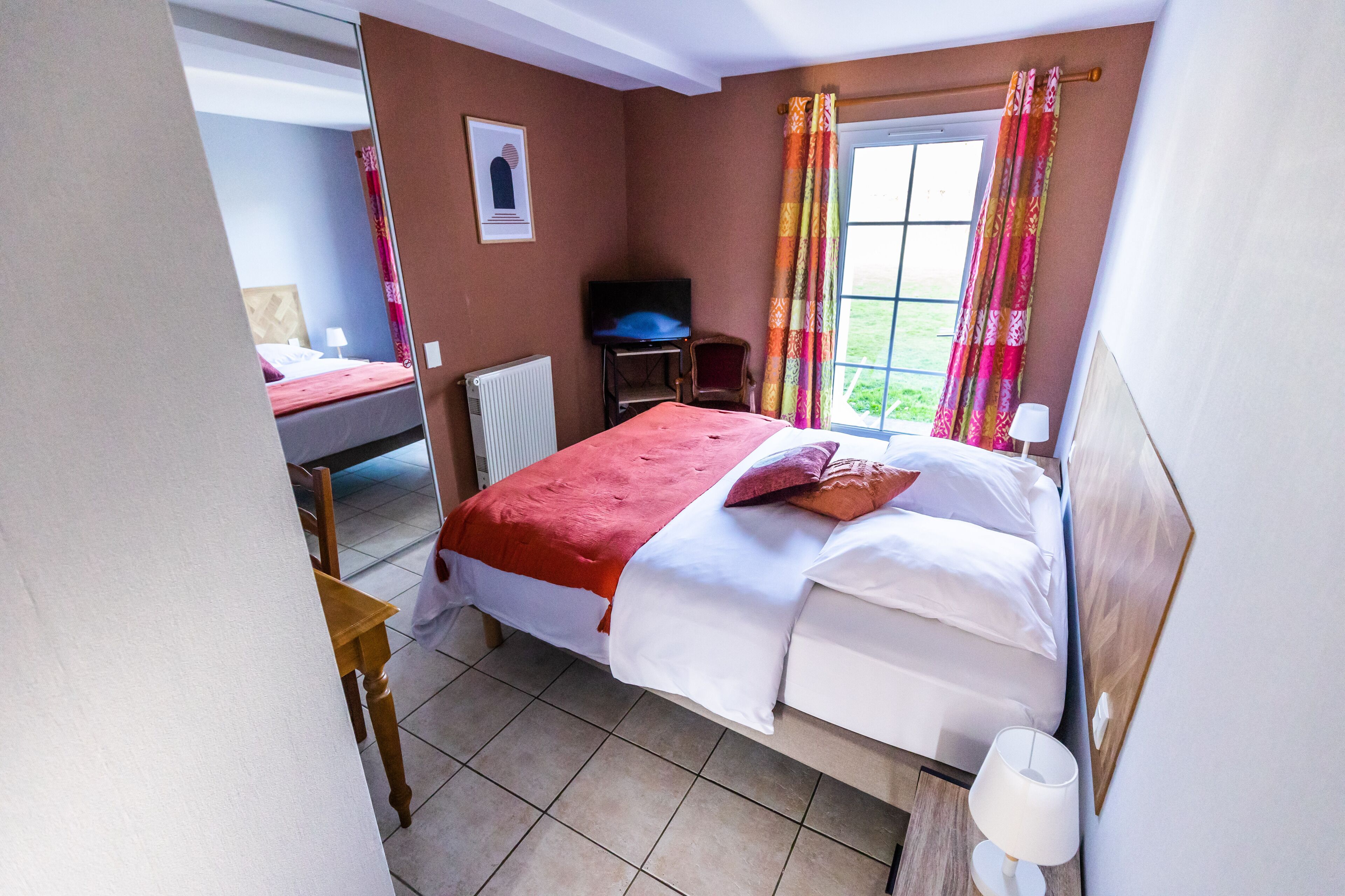 A hotel room with a bed, a desk, a chair, a TV, and a window with curtains.