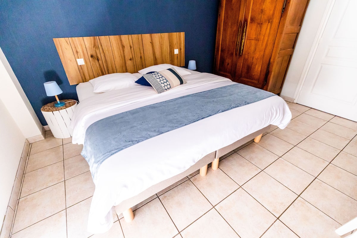Cama bem arrumada com cabeceira de madeira, luminária na mesa de cabeceira e mesa de cabeceira com abajur.