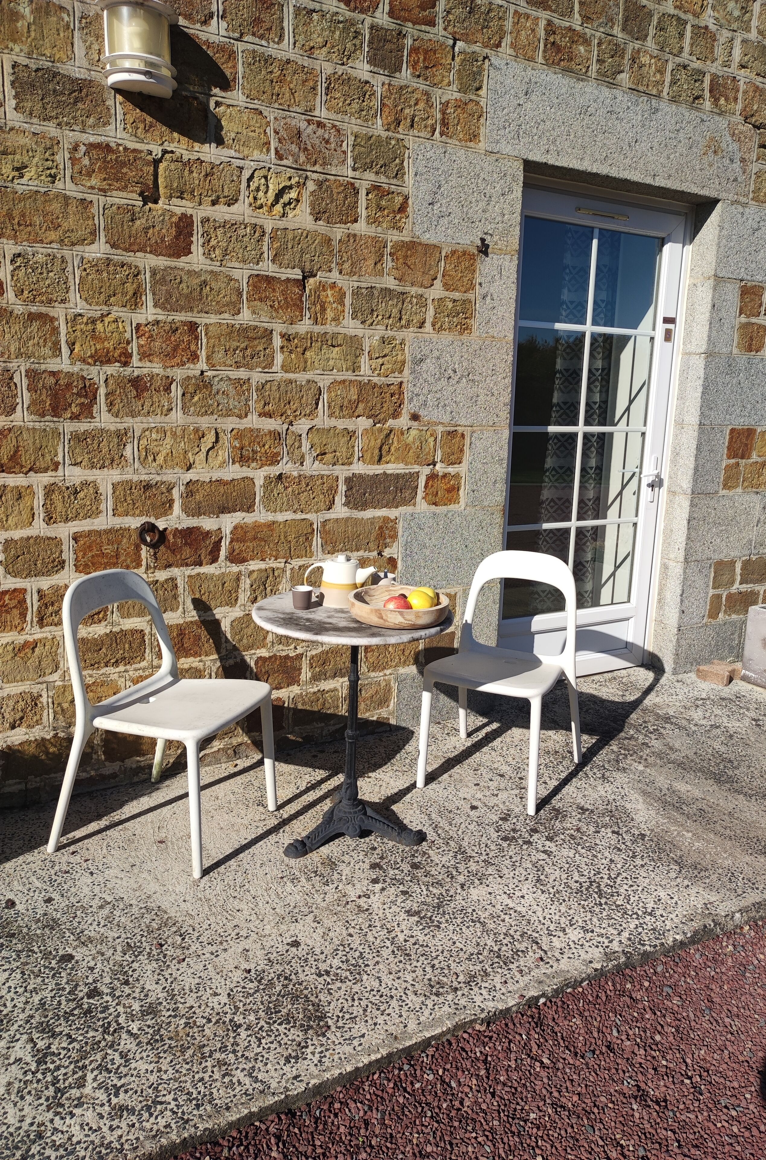A small outdoor seating area with two white plastic chairs and a round table, a brick wall, and a glass door.