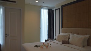 A hotel room with a large bed, a wooden headboard, a bedside table with a phone, and a window with curtains. - Giia Sanno Menteng (Jakarta)